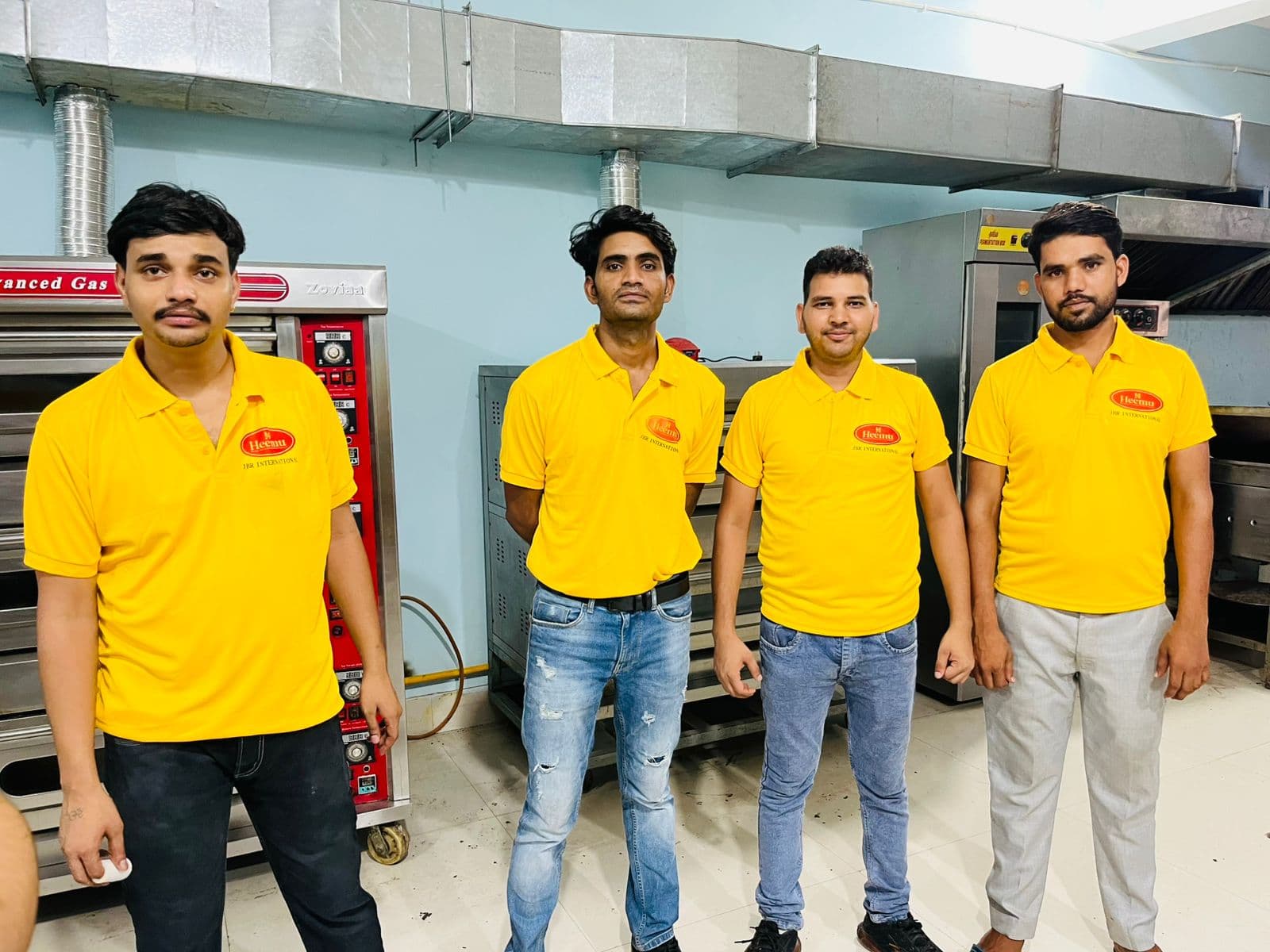 Four JBR bakery staff members in yellow uniforms in front of gas ovens