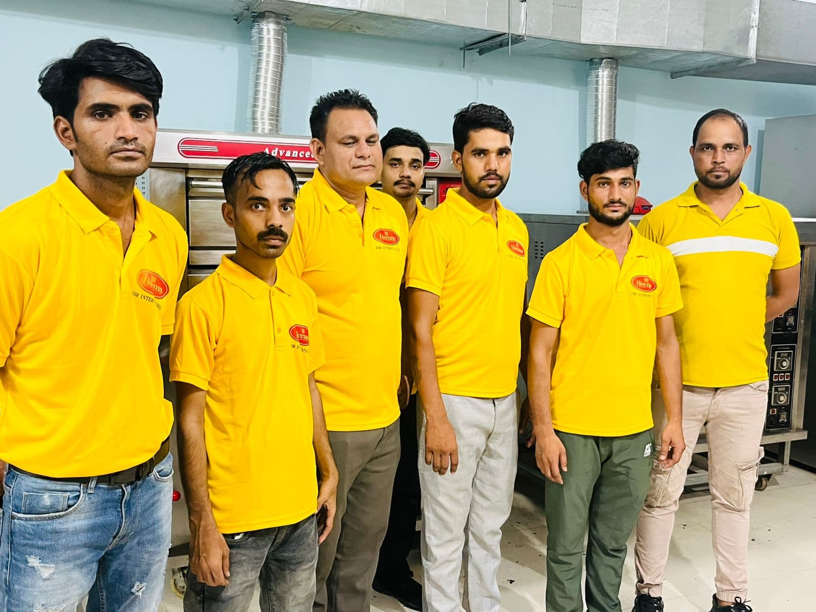 JBR bakery team members in yellow uniforms standing beside the oven line