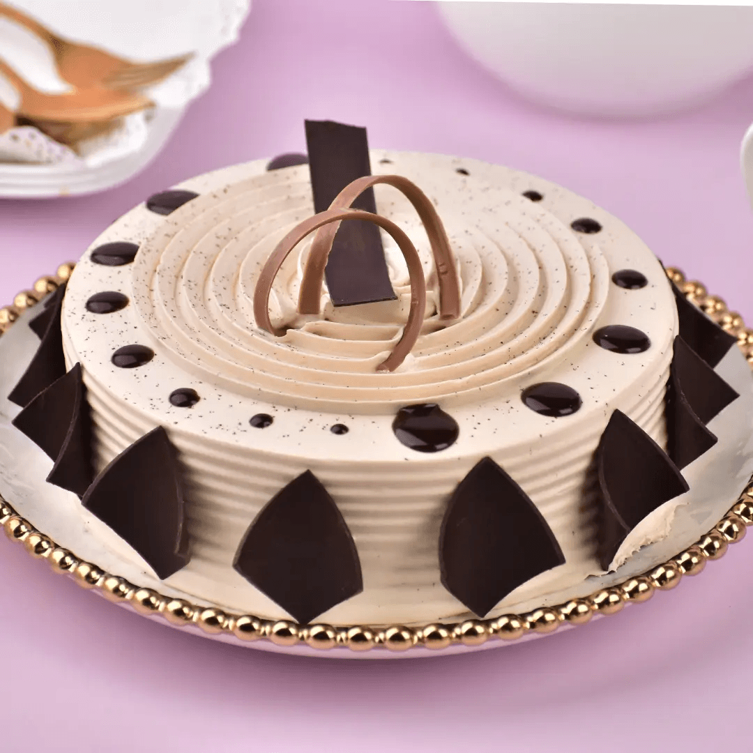 Coffee cream cake with chocolate curls and dark chocolate shard garnish on a gold-rimmed plate
